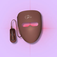 A red light therapy mask with a brownish-gray frame and pink light emitting panels, connected to a controller via a cable.